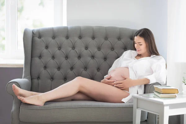 Mladá docela těhotná žena sedí na gauči doma — Stock fotografie