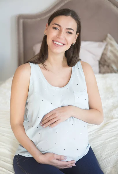 Έγκυος γυναίκα που κάθεται στο εσωτερικό στο κρεβάτι — Φωτογραφία Αρχείου