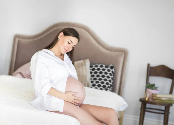 Беременная женщина в помещении сидит на кровати — стоковое фото