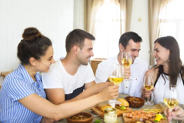 Amigos con vino blanco brindando sobre mesa servida con comida —  Fotos de Stock