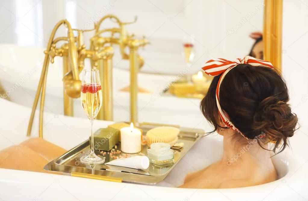 Attractive girl relaxing in bath on light background 