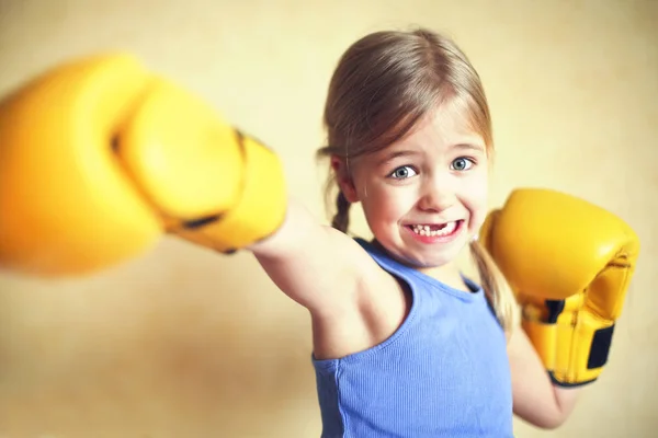 Маленькая девочка в жёлтых боксёрских перчатках над жёлтой стеной — стоковое фото