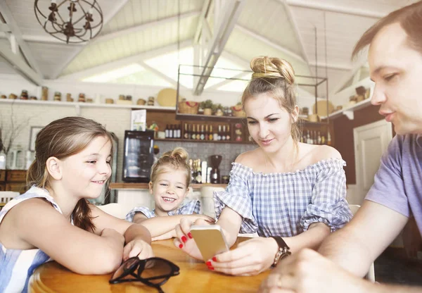 Glückliche Familie mit zwei Töchtern beim Abendessen und Smartphone — Stockfoto