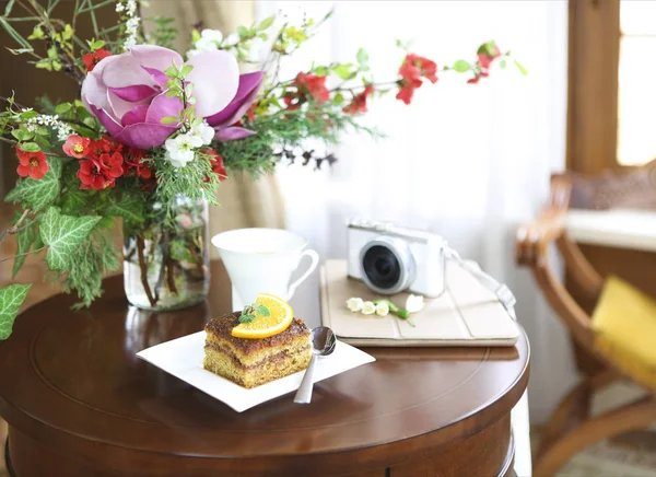 Gâteau au chocolat, thé, tablette, appareil photo et bouquet de fleurs — Photo