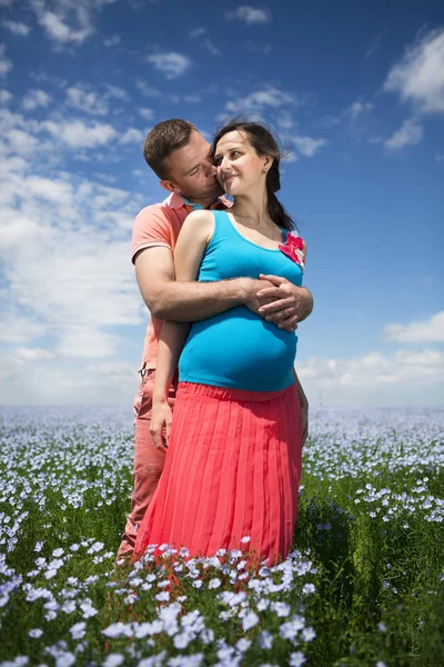 Молодая красивая беременная пара на льняном поле — стоковое фото