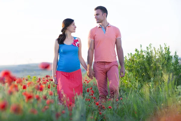 Young beautiful pregnant couple in poppy field — Stock Photo, Image