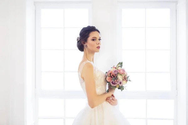 Schöne brünette Frau mit Blumenstrauß posiert in einem Brautkleid — Stockfoto