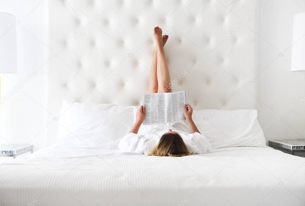 Happy woman reading a magazine in the bed 