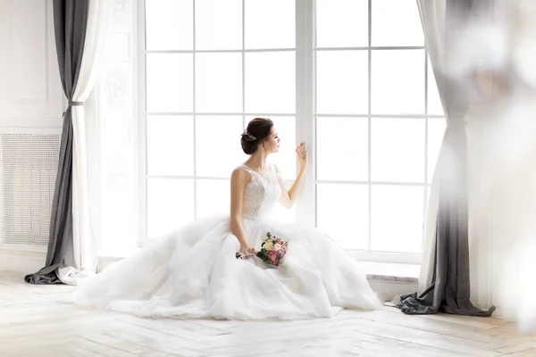 Bella donna bruna con bouquet in posa in un abito da sposa — Foto Stock