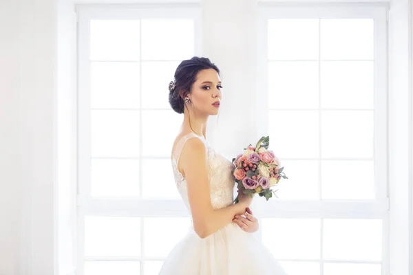 Bella donna bruna con bouquet in posa in un abito da sposa — Foto Stock