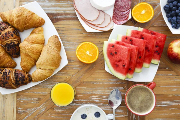 Koffie met fruit, cornflakes en croissant op houten tafelblad — Stockfoto