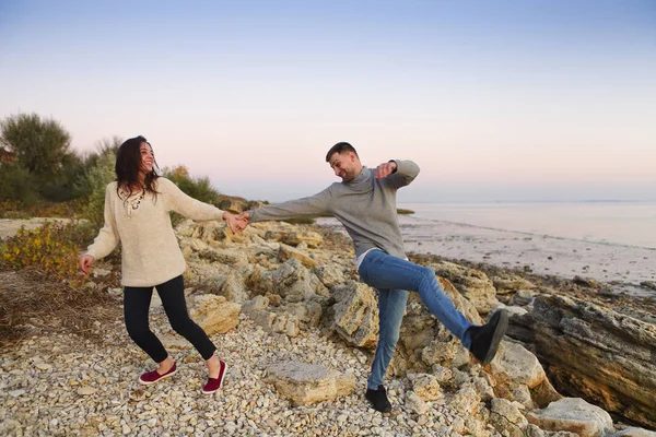 Pareja joven en la costa rocosa en la puesta del sol —  Fotos de Stock