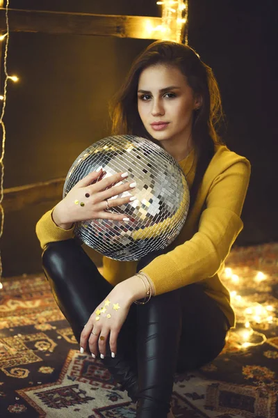 Beautiful young girl in yellow sweater holding disco ball — Stock Photo, Image