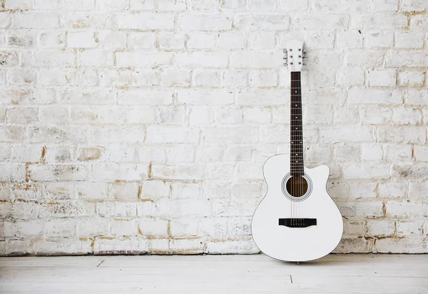 Guitarra blanca acústica apoyada sobre una pared blanca en una r vacía — Foto de Stock