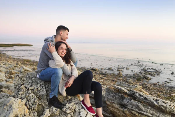 Молода пара на скелястому морі на заході сонця — стокове фото