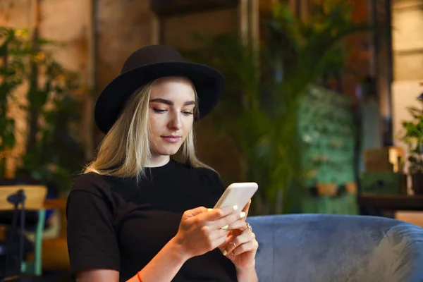 Blond girl in white jeans skirt, blouse and black hat, sitting a — Stockfoto