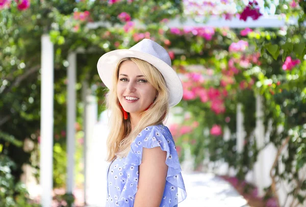 Blond girl in straw hat in front of pink bougainvillea flowers — 스톡 사진