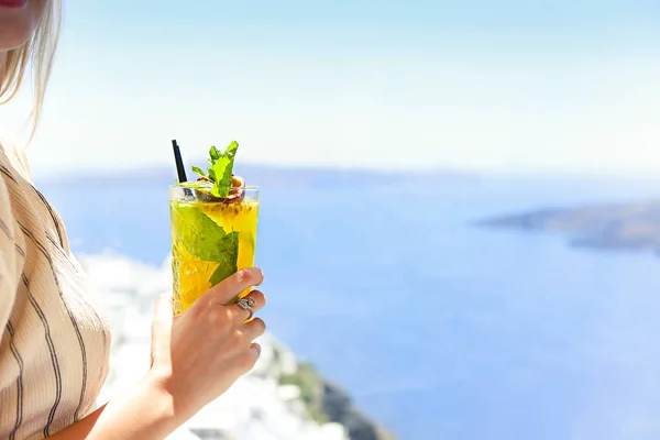 Mujer sosteniendo una copa de cóctel de maracuyá en Santorini bac —  Fotos de Stock