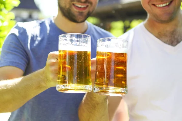 Close up of two young men in casual wear stretching out glasses — Stockfoto