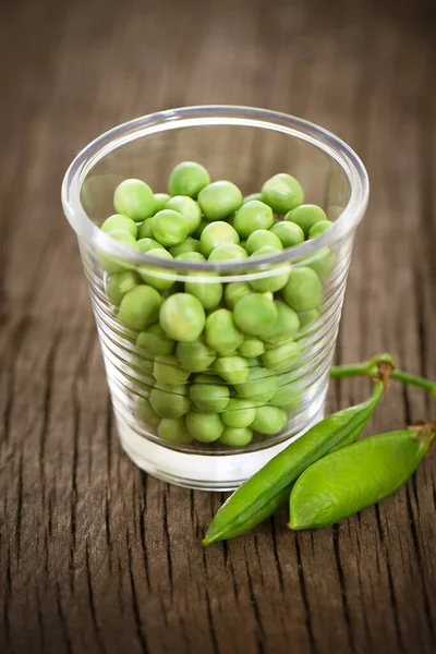 素朴なテーブルの上に小さなガラスの新鮮な緑のエンドウ豆 — ストック写真