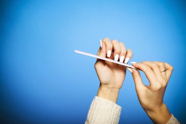 Kırpılmış kadın mavi zeminde uzun tırnaklarını törpülüyor