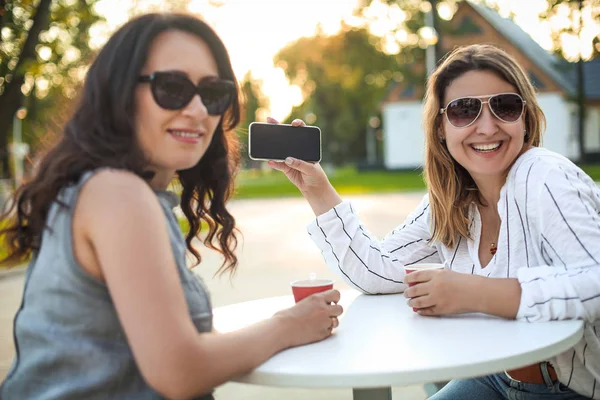 Весёлые взрослые женщины с кофе и мобильным телефоном на улице — стоковое фото