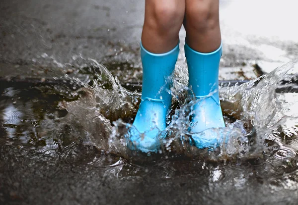 Criança usando botas de chuva azul pulando em um pudim — Fotografia de Stock