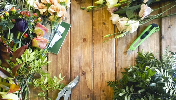 Diverses fleurs et feuilles avec des outils professionnels de fleuriste sur la table en bois — Photo