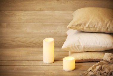 Evdeki sıcaklık ve konforun sembolü olarak, yastıklı ve mumlu sıcacık arka plan ve bulanık ahşap duvarlar.