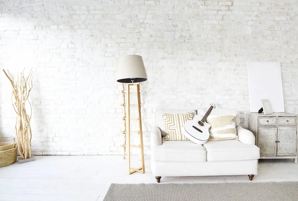 Moda amaçlı geniş çatı katında lamba ve dolap arasında beyaz tuğla duvara dayalı gitarlı kanepe