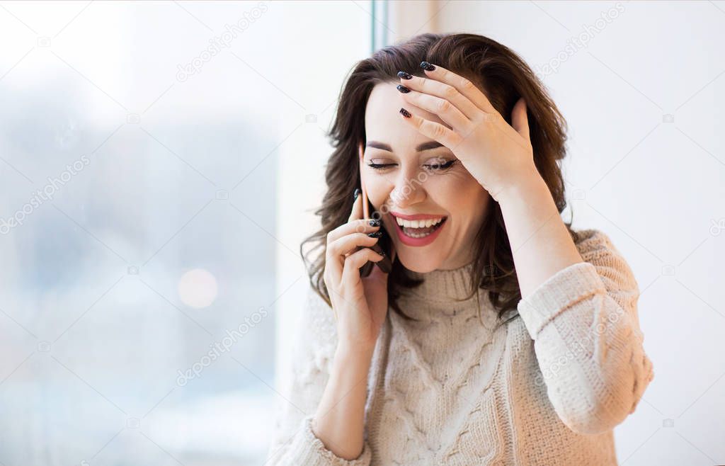 Side view of female in casual knitted sweater with stylish black manicure using mobile phone 