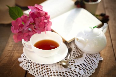 Kırmızı çay ve beyaz seramik çaydanlığın yukarısından ahşap masa üzerinde pembe çiçekler ve açık bir kitap.