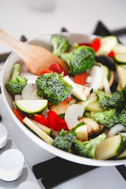 Taze brokoli dilimleri, kabak domatesleri, tavada patlıcan ve ahşap spatula.