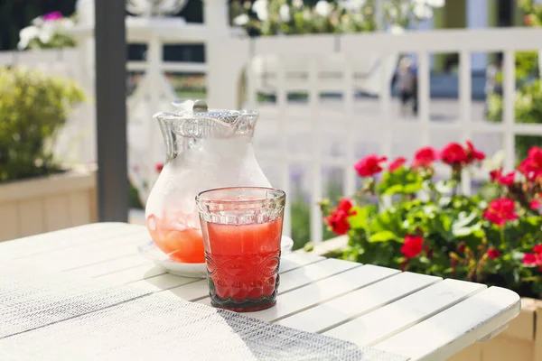 夏日阳光明媚的时候 从上面的玻璃杯里 可以喝到新鲜的红葡萄酒 还可以在花园里的木制白桌子上喝到冷饮 — 图库照片