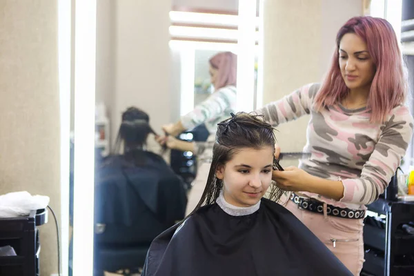 Crop hairstylist using comb and scissors to cut hair of happy female client during work in salon