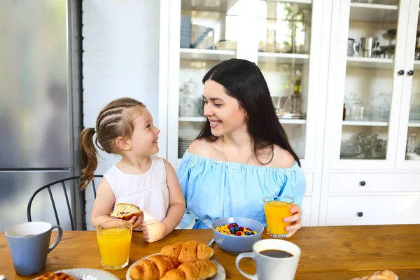 Tatmin olmuş genç anne ve kız kahvaltı kaseleri ve kruvasanlarla masada oturup birbirlerine bakıyorlar.