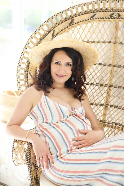 夢のような妊娠中の女性で夏服見ながら離れて休憩で快適なウィッカーアームチェアオンテラス — ストック写真