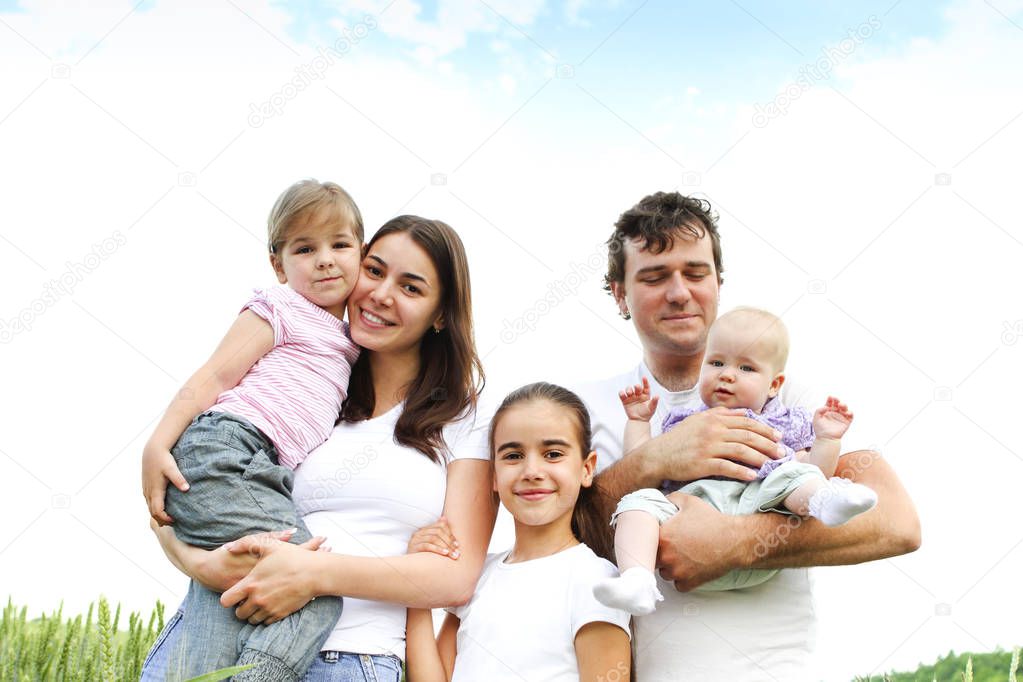 Happy family of parents and three girls hugging and smiling at camera in summer field