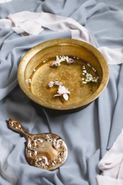 Taze çiçek başları ve kaliteli el aynası ile yüksek açılı kahverengi su kabı şeffaf pastel renkli kumaşlar ve yüz yıkama için hazırlanmış yeşil yapraklar ve çiçekler arasında.