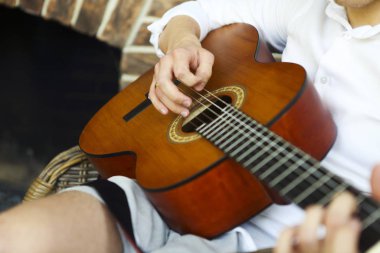 Tanımlanamayan erkek akustik gitar çalarken koltukta oturup evde dinleniyor.