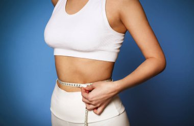 Güzel, sıska bir kız, ince belini, mavi sırt çantasından mezura ile ölçüyor. Spor ve Sağlıklı Yaşam Konsepti 