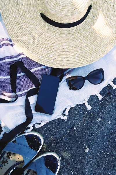黒砂のビーチで毛布の上に電話と麦藁帽子と女性のサングラスを見る — ストック写真