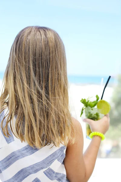 夏の晴れた日にビーチで休んで冷たいモヒートのガラスと認識できない女の子のバックビュー — ストック写真