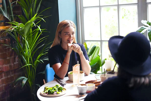 Smiling blond woman on meeting with female friend in cafe having refreshing drinks and healthy meal for lunch