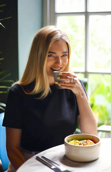 Gelukkig Jong Vrouwtje Met Kopje Verse Koffie Glimlachend Aan Tafel — Stockfoto