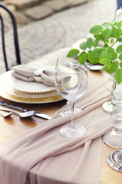 Bahçede romantik bir buluşma sırasında şarap kadehlerinin yanına yuvarlak güller konmuş mum ve vazo.
