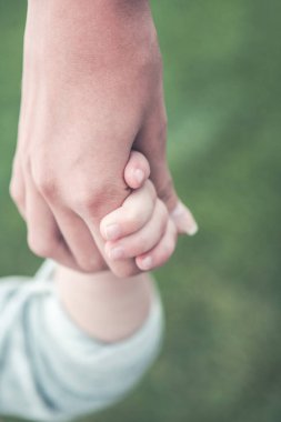 Yazın parkta yeşil çimlerde yan yana dururken küçük bir çocuğun elini tutan isimsiz bir kadın.