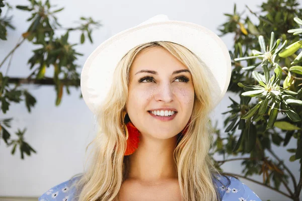 Pozitif sarışın kadın şapkalı ve şık kırmızı küpeli yaz günü bahçede duruyor.