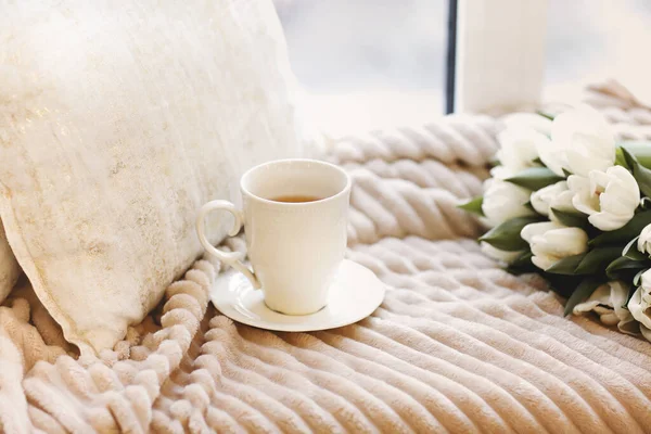 新鮮な白いチューリップとコーヒーの白いカップの花束は 明るい寝室でベージュの豪華な毛布と枕で居心地の良いベッドに置かれます — ストック写真