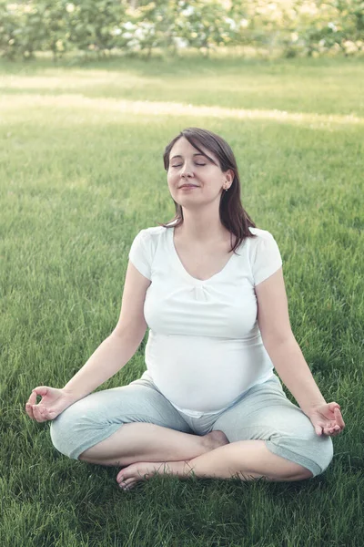 妊娠中の女性は夏の庭でハスの位置に座って瞑想 — ストック写真